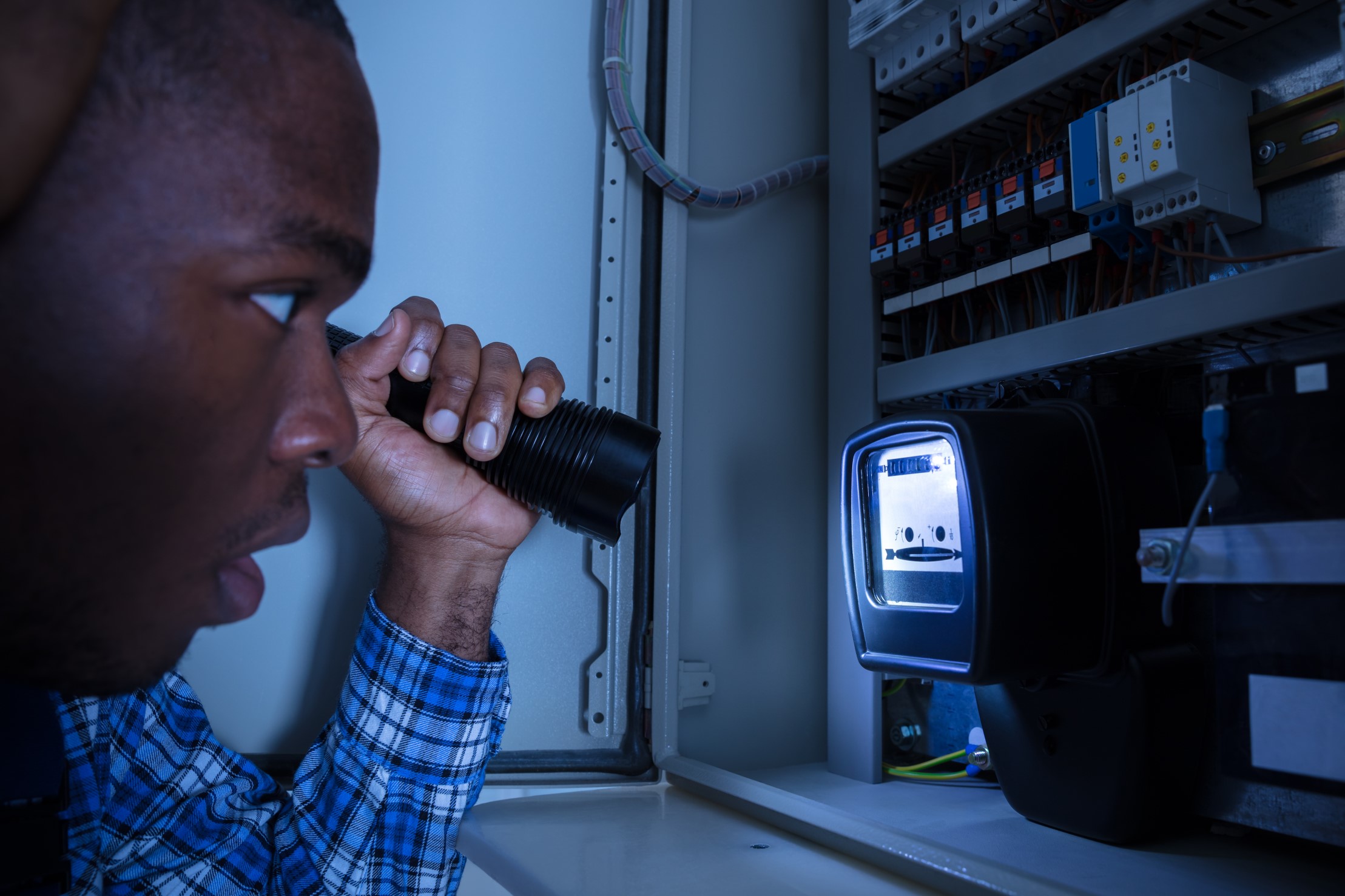 A man looking at a fuse box with a torch