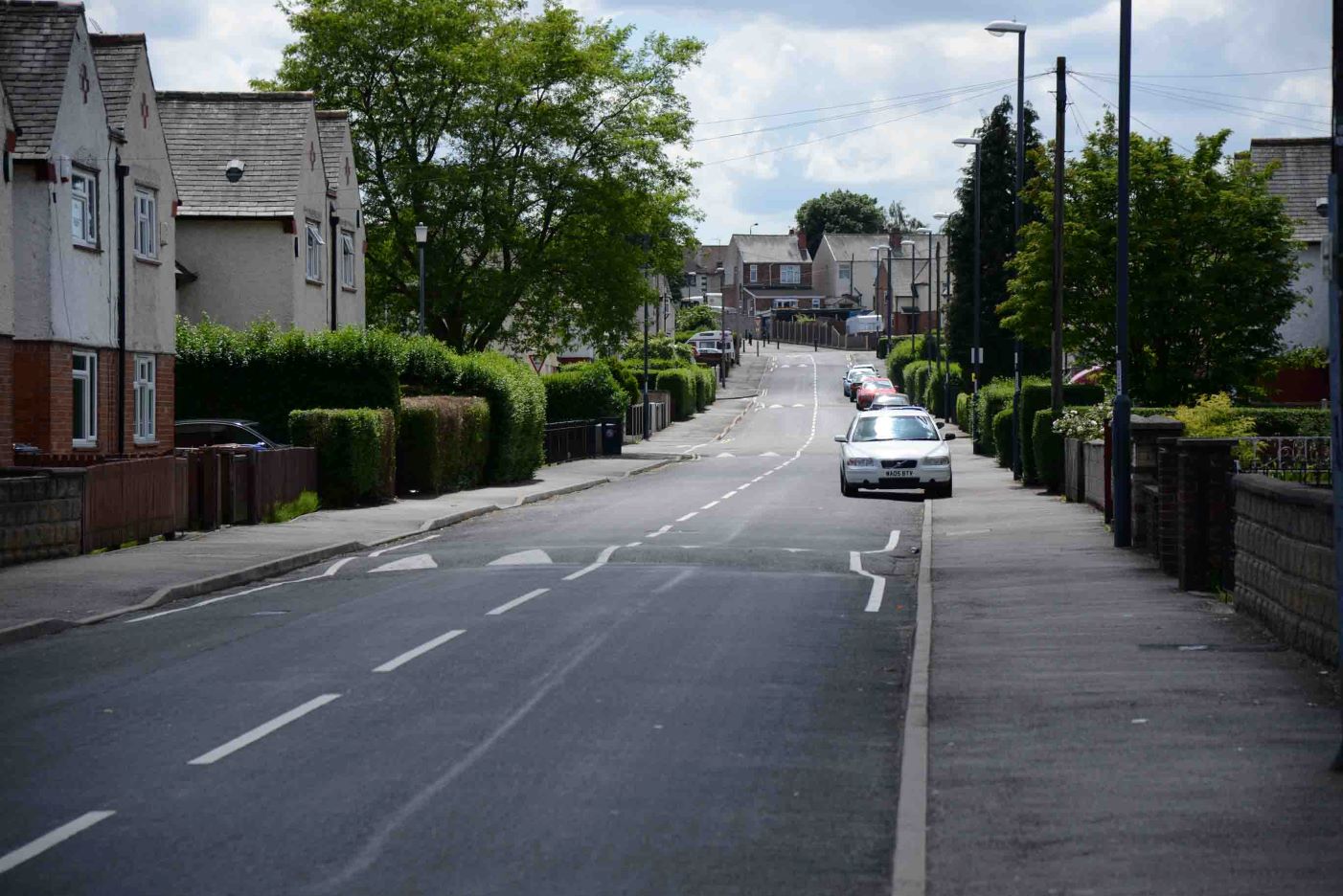 Wide angle shot of a street with houses on either side and curb mounted car in the distance