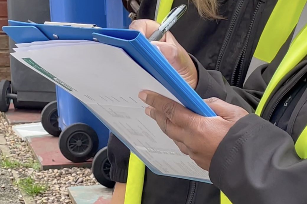 Close up photo of someone in a high visibility vest making notes on a blue clipboard